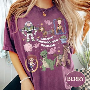 Pu&ograve; includere: T-shirt color bacca con personaggi dei cartoni animati di Toy Story. Il design include Buzz Lightyear, Woody, Jessie, Rex, Hamm, Slinky Dog, Bullseye e un alieno, con la scritta "You've Got a Friend in Me."