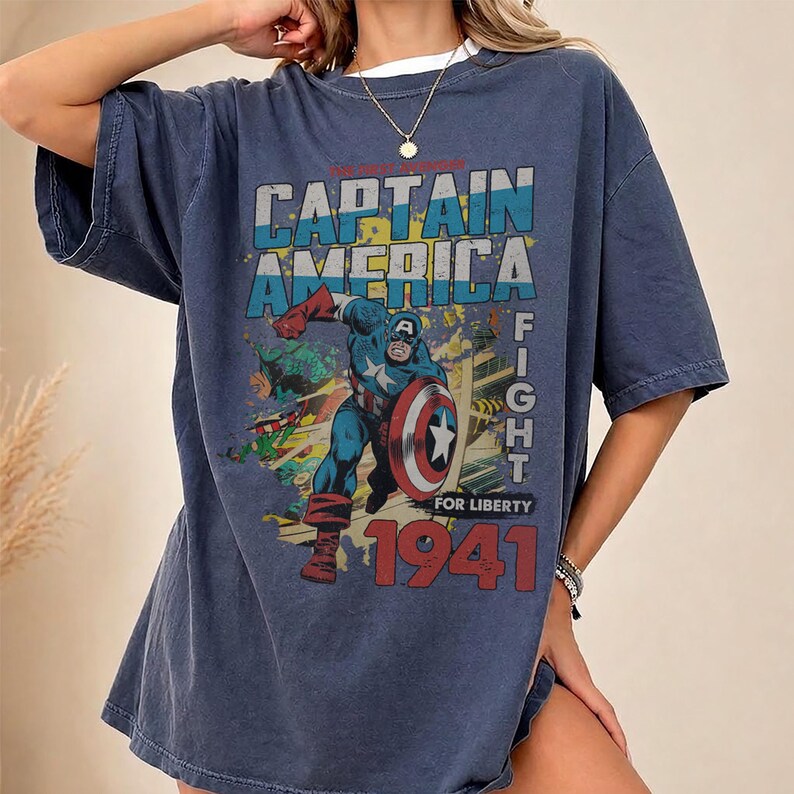 Puede incluir: Una camiseta de manga corta de color azul oscuro con un estampado gr&aacute;fico de Capit&aacute;n Am&eacute;rica en una pose din&aacute;mica con un escudo. El texto dice CAPTAIN AMERICA FIGHT FOR LIBERTY 1941 en letras negritas. El dise&ntilde;o incluye acentos en rojo, blanco y azul.