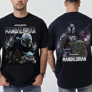 Puede incluir: Camiseta negra con un gr&aacute;fico de The Mandalorian y Grogu de Star Wars. El frente muestra a los personajes con el logo del programa. La parte posterior muestra al Mandaloriano y Grogu contra un fondo espacial.