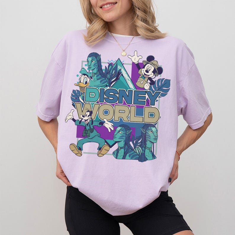 Puede incluir: Una camiseta de manga corta de color morado claro con un estampado gr&aacute;fico de personajes de Disney, incluyendo a Mickey Mouse, el Pato Donald, Goofy y figuras Na'vi de Avatar. El texto "DISNEY WORLD" aparece en el centro en letras azules y doradas.