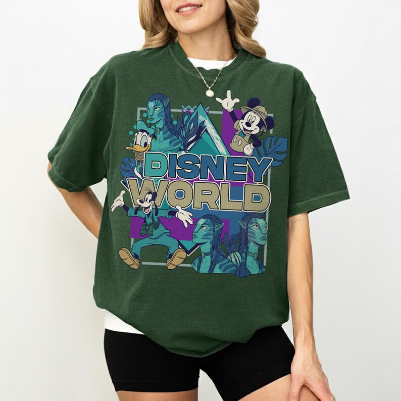 Puede incluir: Una camiseta de manga corta de color verde oscuro con un estampado gr&aacute;fico que incluye el texto "DISNEY WORLD" en azul y dorado. El dise&ntilde;o presenta ilustraciones de Mickey Mouse, Donald Duck, Goofy y personajes azules de la franquicia Avatar.
