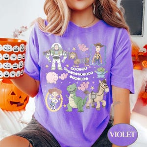 Pu&ograve; includere: Una maglietta viola con personaggi dei cartoni animati del film Toy Story. La maglietta include immagini di Buzz Lightyear, Woody e altri personaggi, con la scritta "You've Got a Friend in Me".