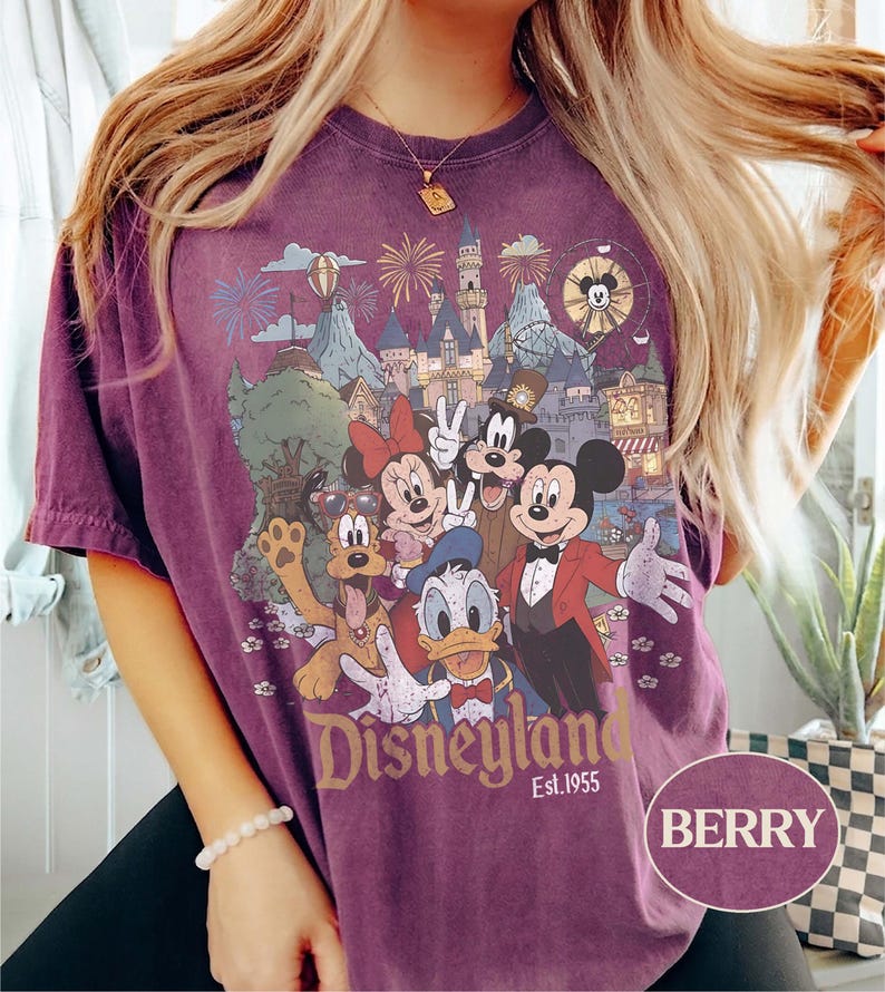 Puede incluir: Camiseta de color bayas con un gr&aacute;fico de Disneyland con Mickey Mouse, Minnie Mouse, Donald Duck y Goofy. El gr&aacute;fico incluye un castillo, fuegos artificiales y el texto "Disneyland Est. 1955". La camiseta tiene mangas cortas y cuello redondo.