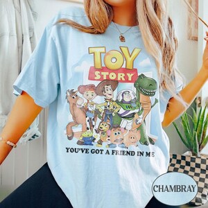 Puede incluir: Camiseta azul claro con la inscripci&oacute;n "TOY STORY" sobre un dibujo de los personajes de la pel&iacute;cula. El texto "YOU'VE GOT A FRIEND IN ME" est&aacute; debajo. La camiseta es de estilo casual.