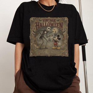 May include: A black short-sleeve t-shirt featuring a rectangular graphic print with the text VINTAGE HALLOWEEN, EST. 1937, and CELEBRATION. The illustration depicts a tall skeletal figure and a mouse character in a spooky landscape with bats.