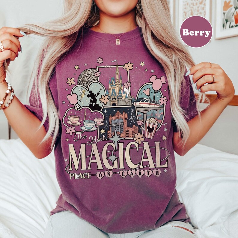 Puede incluir: Camiseta color bayas con un dise&ntilde;o gr&aacute;fico que muestra im&aacute;genes ic&oacute;nicas de parques tem&aacute;ticos, como un castillo, tazas de t&eacute; y un monorra&iacute;l. El texto "The Most Magical Place on Earth" se muestra de forma destacada. La camiseta es informal y c&oacute;moda.