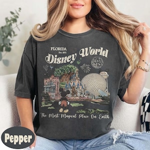 Może przedstawiać: Ciemnoszara koszulka z grafiką w stylu vintage z Disney World. Projekt zawiera napisy "Florida Disney World Est. 1971" oraz obrazy z parku, w tym Myszka Miki, zamek i Spaceship Earth.