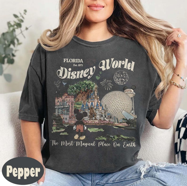 Może przedstawiać: Ciemnoszara koszulka z grafiką w stylu vintage z Disney World. Projekt zawiera napisy "Florida Disney World Est. 1971" oraz obrazy z parku, w tym Myszka Miki, zamek i Spaceship Earth.