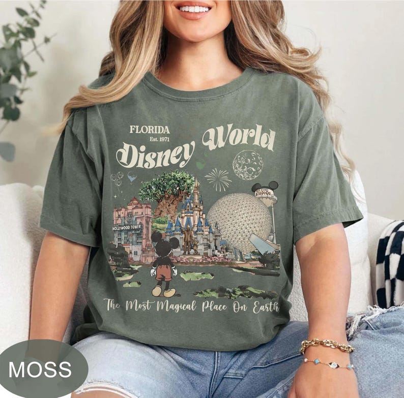 Może przedstawiać: Zielona koszulka w kolorze mchu z grafiką Disney World. Projekt zawiera napisy "Florida Disney World" i "The Most Magical Place On Earth", a także ilustracje zabytk&oacute;w parku i Myszki Miki.