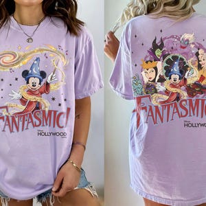 May include: A light purple t-shirt featuring Mickey Mouse as the Sorcerer's Apprentice with the text "FANTASMIC!" in red. The back of the shirt shows Disney villains. The shirt is a relaxed fit.