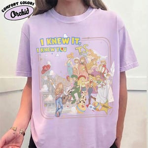May include: A light purple short-sleeve t-shirt featuring a graphic print of multiple illustrated characters in various outfits. The text reads I KNEW IT, I KNEW YOU TS and SHERIFF. The design includes a star, a ball, and a rocket ship within a frame.