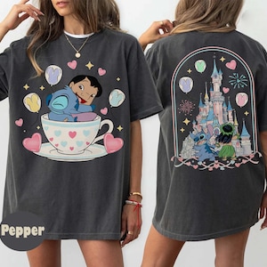 Puede incluir: Camiseta gris oscuro con una ilustraci&oacute;n de dibujos animados de Stitch y Lilo en una taza de t&eacute;, rodeados de corazones y globos. La parte trasera de la camiseta muestra una escena de castillo con Stitch y Lilo. La camiseta tiene un corte holgado.
