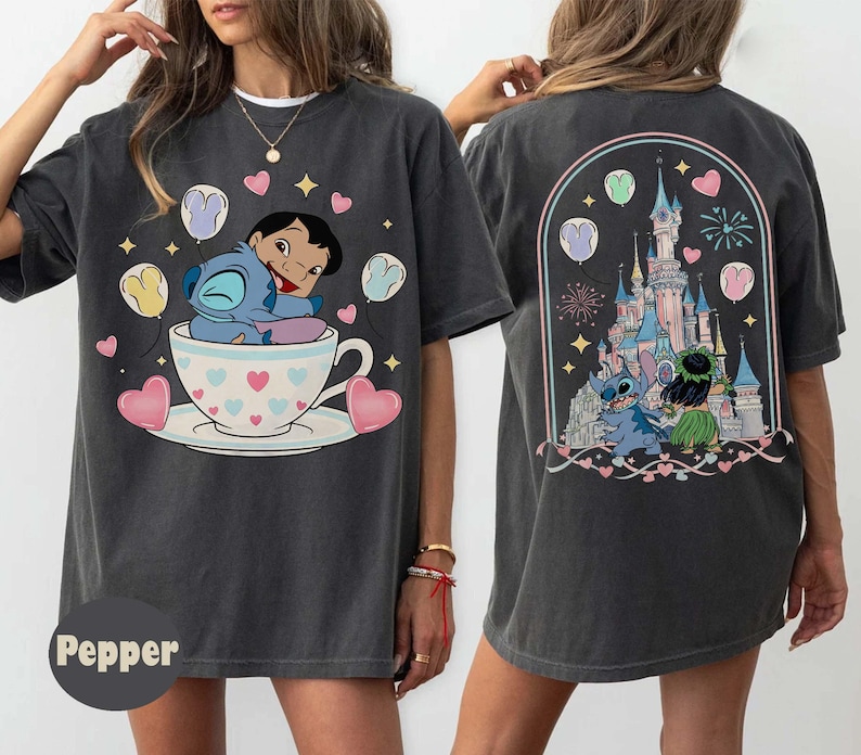 Puede incluir: Camiseta gris oscuro con una ilustraci&oacute;n de dibujos animados de Stitch y Lilo en una taza de t&eacute;, rodeados de corazones y globos. La parte trasera de la camiseta muestra una escena de castillo con Stitch y Lilo. La camiseta tiene un corte holgado.
