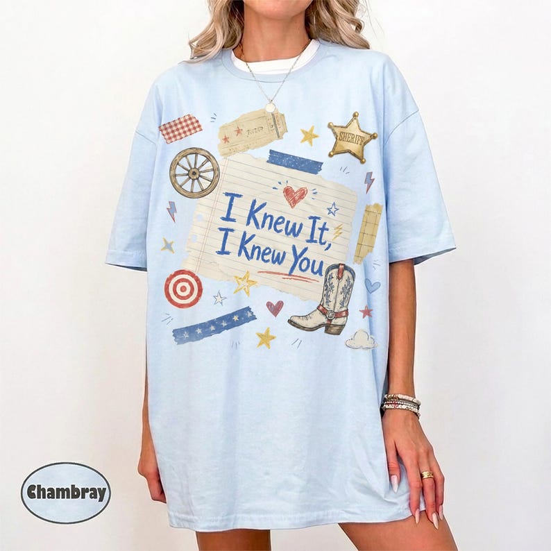 May include: A light blue t-shirt featuring a graphic print of a lined paper sheet with the text "I Knew It, I Knew You" in blue. The design includes a cowboy boot, a sheriff star, a wagon wheel, a target, and various small stars and hearts.