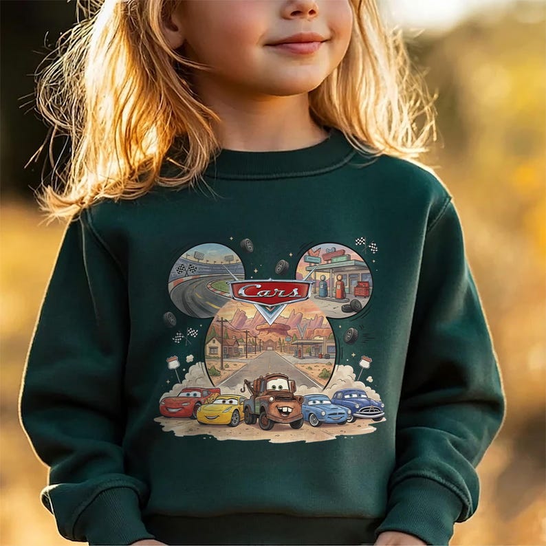 Puede incluir: Una sudadera de manga larga de color verde oscuro con un estampado gr&aacute;fico del logotipo de Disney Pixar Cars y personajes como Rayo McQueen, Mate y otros. El dise&ntilde;o incluye escenas circulares de una pista de carreras y una gasolinera.