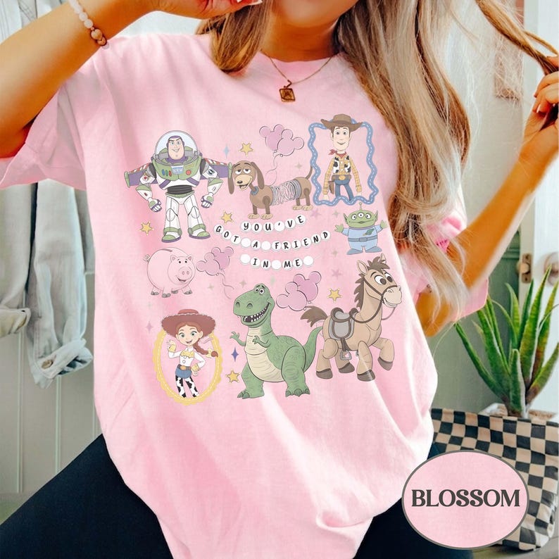 Pu&ograve; includere: T-shirt rosa chiaro con personaggi dei cartoni animati del film Toy Story. Il design include Buzz Lightyear, Woody, Jessie, Rex e altri personaggi, con la scritta "You've Got a Friend in Me."