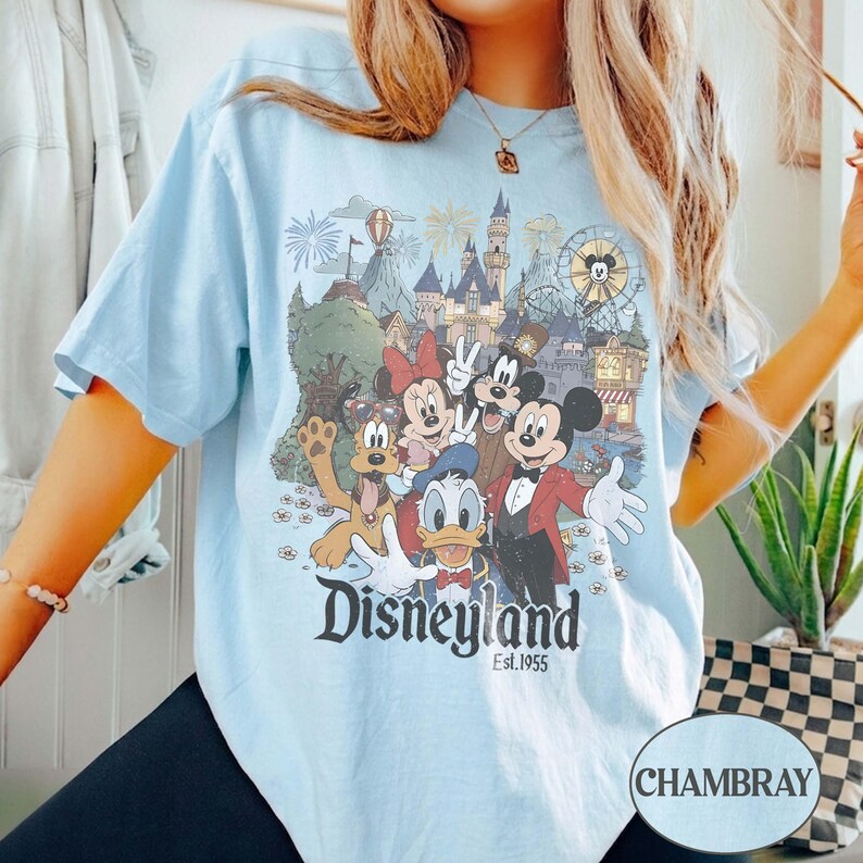 Puede incluir: Camiseta azul claro con un gr&aacute;fico de Disneyland con Mickey Mouse, Minnie Mouse y otros personajes de Disney. El gr&aacute;fico incluye el logotipo de Disneyland y el texto "Est. 1955". Una camiseta informal de manga corta.