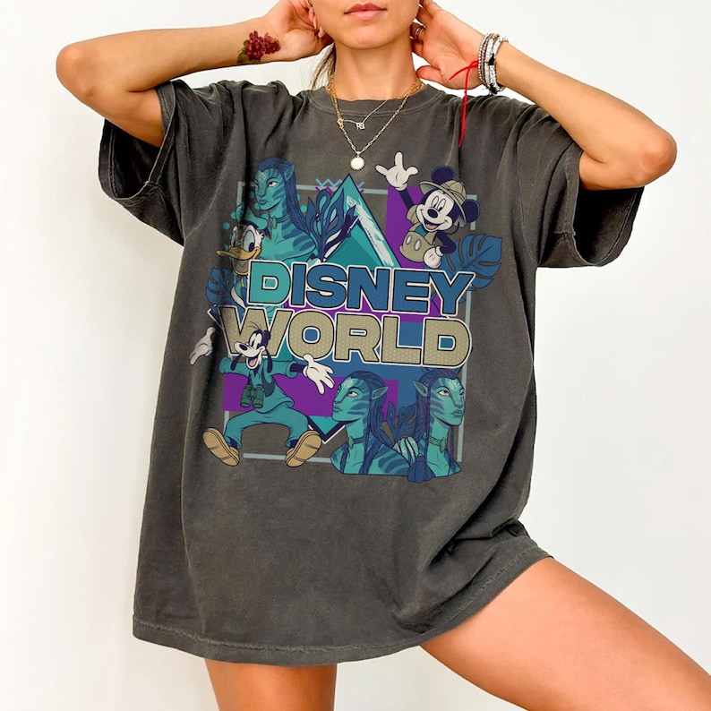 Puede incluir: Una camiseta de manga corta gris carb&oacute;n con un estampado gr&aacute;fico que incluye el texto DISNEY WORLD. El dise&ntilde;o presenta ilustraciones de Mickey Mouse, Goofy, el Pato Donald y personajes de Avatar sobre un fondo geom&eacute;trico.