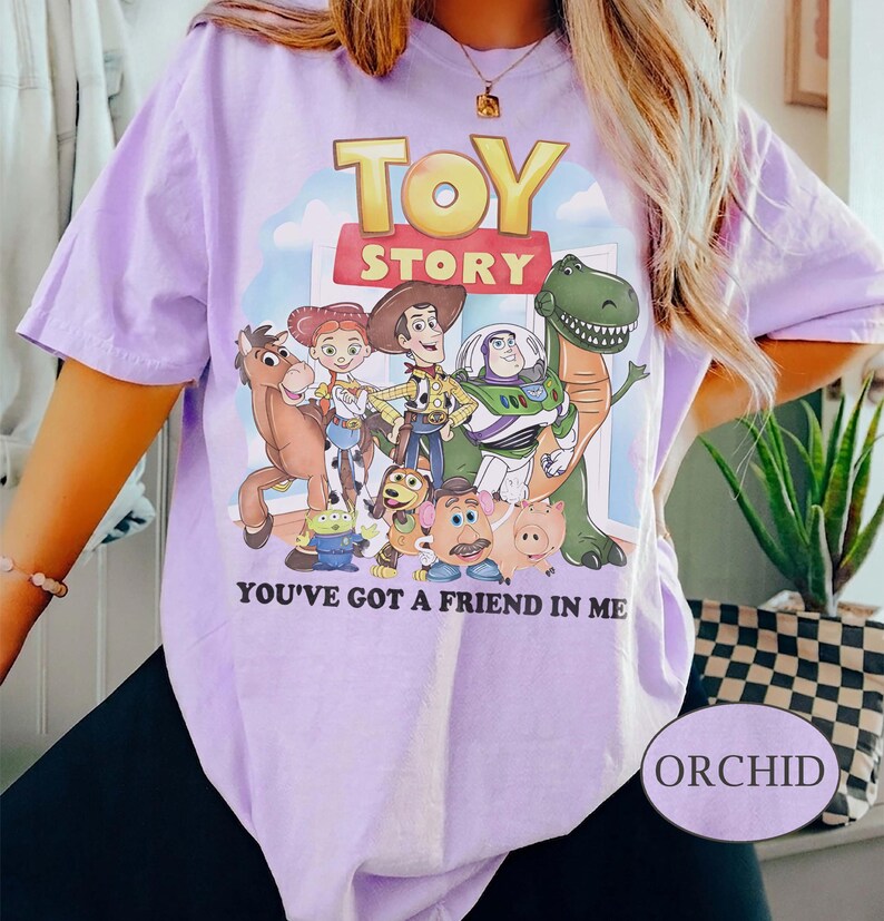 Puede incluir: Camiseta color orqu&iacute;dea con un gr&aacute;fico de personajes de la pel&iacute;cula animada "Toy Story". El dise&ntilde;o incluye a Woody, Buzz Lightyear y otros personajes, con el texto "TOY STORY" y "YOU'VE GOT A FRIEND IN ME". La camiseta tiene mangas cortas.
