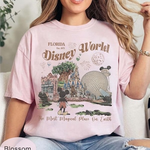 Może przedstawiać: Jasnor&oacute;żowa koszulka z grafiką Disney World na Florydzie. Projekt zawiera napis "Florida Disney World Est. 1971" oraz ilustrację Myszki Miki, Drzewa Życia i Spaceship Earth. Zawiera r&oacute;wnież tekst "The Most Magical Place On Earth".