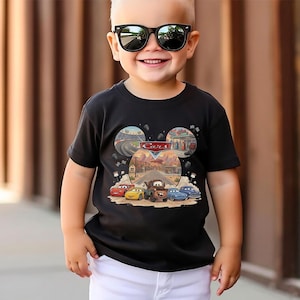 Puede incluir: Una camiseta negra de manga corta con un estampado gr&aacute;fico de los personajes y paisajes de Disney Pixar Cars. El dise&ntilde;o incluye un logotipo central de Cars, una pista de carreras, una gasolinera y una carretera des&eacute;rtica con cinco veh&iacute;culos.
