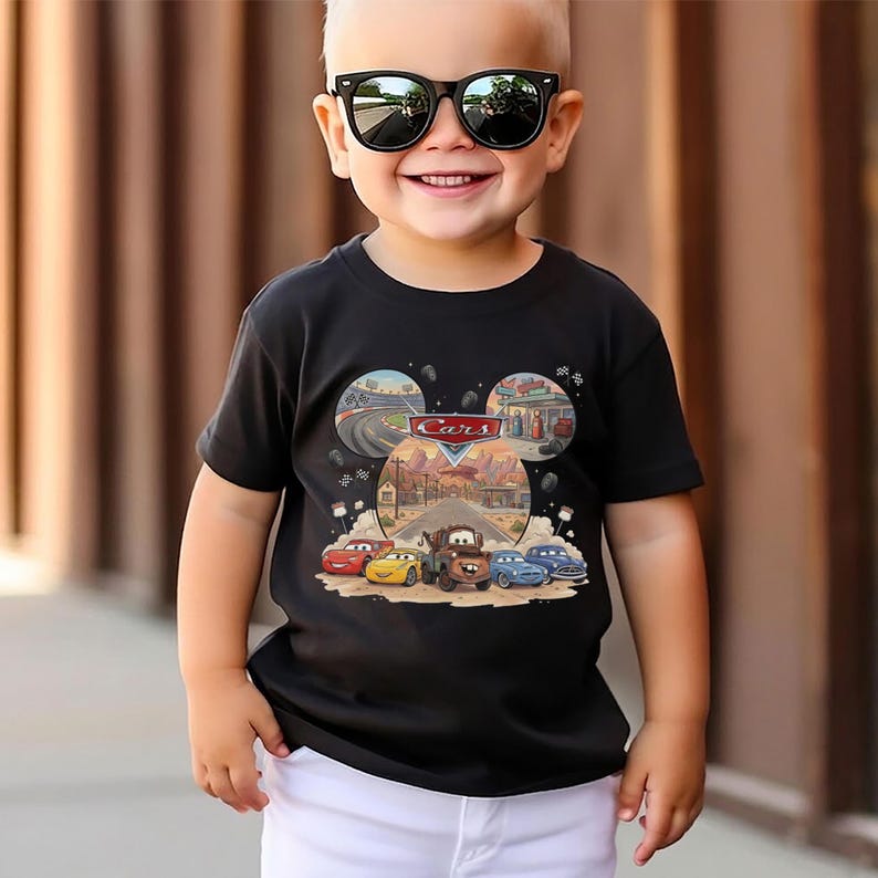 Puede incluir: Una camiseta negra de manga corta con un estampado gr&aacute;fico de los personajes y paisajes de Disney Pixar Cars. El dise&ntilde;o incluye un logotipo central de Cars, una pista de carreras, una gasolinera y una carretera des&eacute;rtica con cinco veh&iacute;culos.