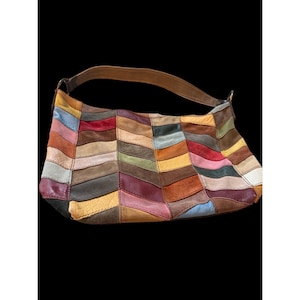 Puede incluir: Un bolso de hombro estilo hobo construido con un mosaico de piezas de cuero multicolor dispuestas en un patrón de chevrón. El bolso cuenta con una sola correa de cuero marrón sujeta con herrajes metálicos y muestra varios tonos de rojo, azul, amarillo, verde y marrón.