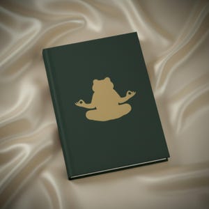 Peut inclure: Un journal vert foncé avec une illustration dorée d'une grenouille en position de méditation. Le journal est rectangulaire et possède une couverture lisse. La grenouille est centrée.