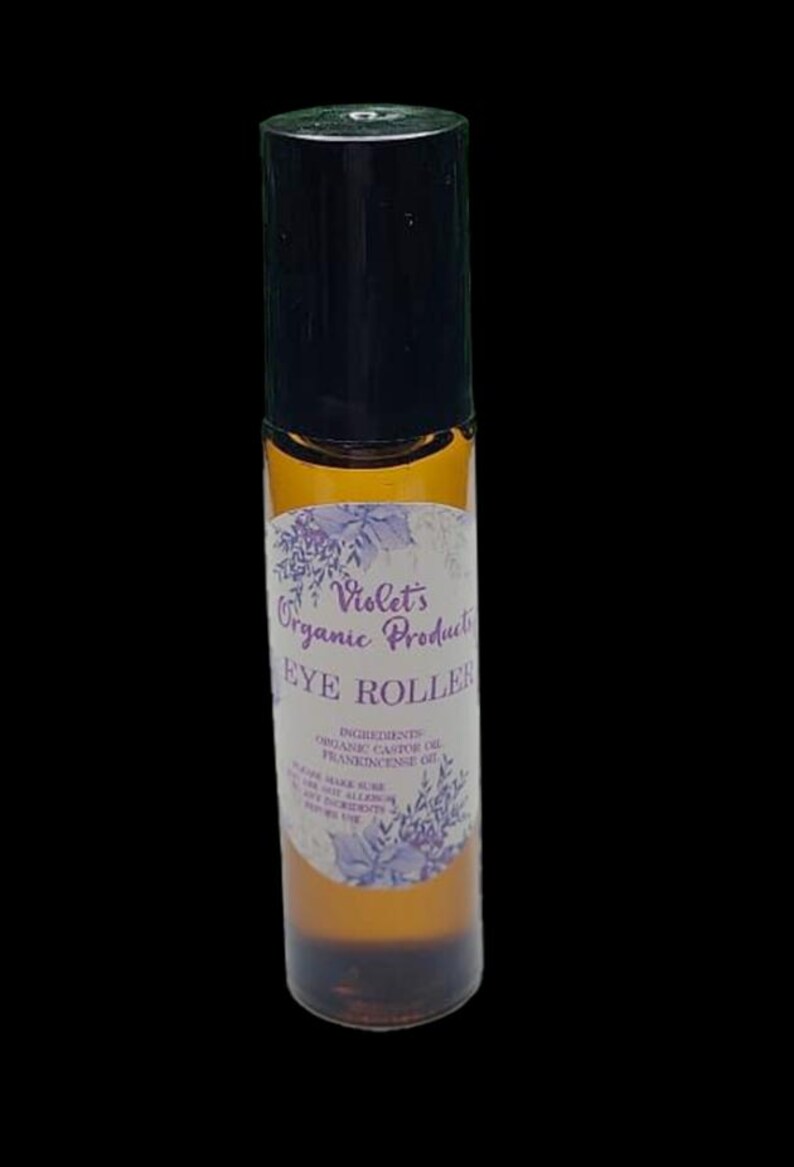 Pu&ograve; includere: Un flacone roll-on per occhi in vetro marrone con tappo nero. L'etichetta recita "Violet's Organic Products EYE ROLLER" con un design floreale. Gli ingredienti includono olio di ricino biologico e olio di incenso.