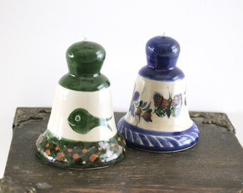 Pode incluir: Dois sinos de cerâmica com desenhos pintados. O sino à esquerda é verde com fundo branco e um desenho de peixe verde. O sino à direita é azul com fundo branco e um desenho floral.
