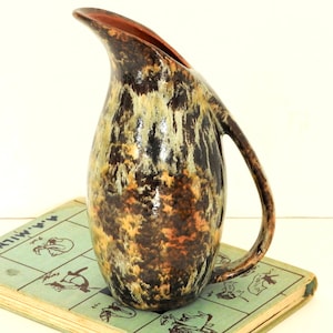 Peut inclure: Un pichet en céramique brun et crème avec un glaçage marbré. Le pichet a une base large et arrondie et un bec étroit. Il a une poignée qui s'incurve vers le haut et au-dessus du pichet.