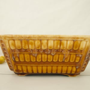 May include: A brown and white ceramic planter with a geometric design. The planter has a rectangular shape with rounded corners and a slightly flared lip.