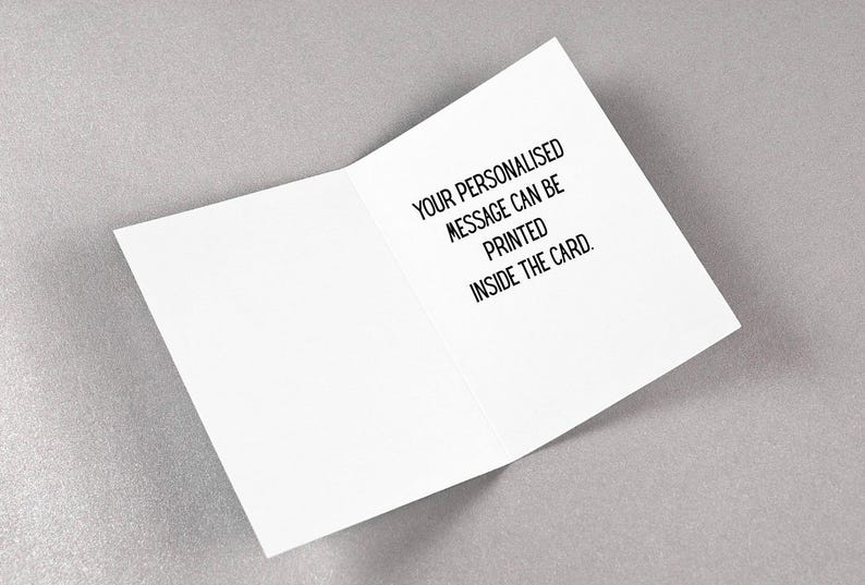 May include: An open white greeting card with black text that reads, "YOUR PERSONALISED MESSAGE CAN BE PRINTED INSIDE THE CARD." The card is on a light gray surface.