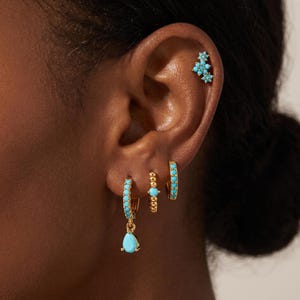 May include: A set of gold-tone earrings featuring turquoise-colored stones. The collection includes a teardrop charm hoop, a beaded hoop with a central stone, a plain turquoise-set hoop, and a small cluster stud earring for the upper ear.