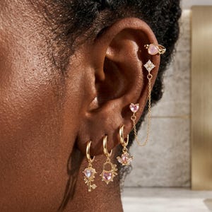 May include: A set of gold-toned earrings featuring a variety of designs including a small heart ear cuff, a star-shaped stud connected by a delicate chain, a heart stud, and three hoop earrings with dangling charms shaped like a key, a heart, and a flower.