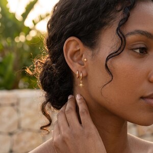 May include: A gold-toned ear jewelry set consisting of a small stud earring featuring a four-pointed star design and a hoop earring with a matching dangling star charm. The jewelry is polished and features a bright, reflective metallic finish.