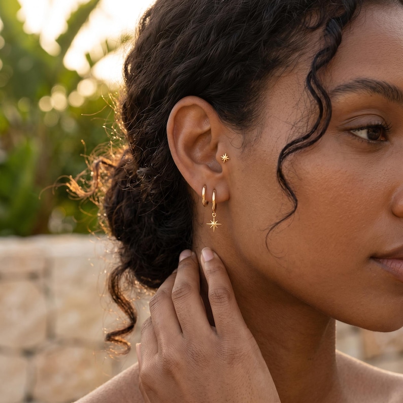 May include: A gold-toned ear jewelry set consisting of a small stud earring featuring a four-pointed star design and a hoop earring with a matching dangling star charm. The jewelry is polished and features a bright, reflective metallic finish.