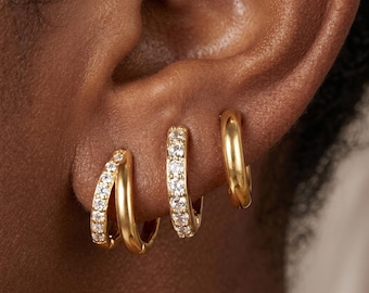 May include: Three gold hoop earrings worn in a row on an earlobe. The first earring is a double hoop with one band featuring clear pavé stones. The second is a single hoop with clear pavé stones. The third is a plain, smooth gold hoop earring.