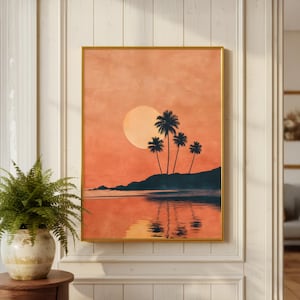 May include: Framed art print depicting a sunset scene with palm trees silhouetted against an orange sky. The artwork shows a beach with the sun reflecting on the water. The print is encased in a gold frame.