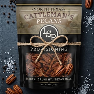 May include: A black bag of Cattleman's Pecans tied with twine, with the text "North Texas" and "Provisioning". The bag contains pecans and is surrounded by pecans, peppercorns, and salt. The net weight is 8 oz.