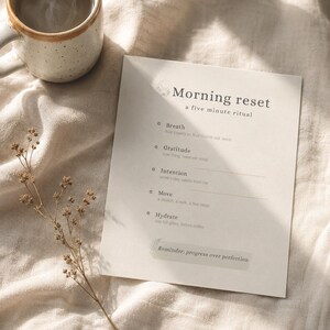 May include: A rectangular white card featuring the text Morning reset a five minute ritual with bulleted prompts for Breath, Gratitude, Intention, Move, and Hydrate, plus a bottom banner stating Reminder: progress over perfection.