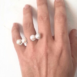 May include: A silver ring with three white pearls on a hand. The ring is designed to be worn on two fingers.