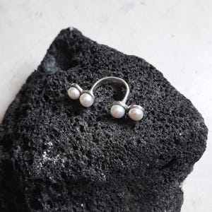 May include: A silver ring with four white pearls set in a curved design.