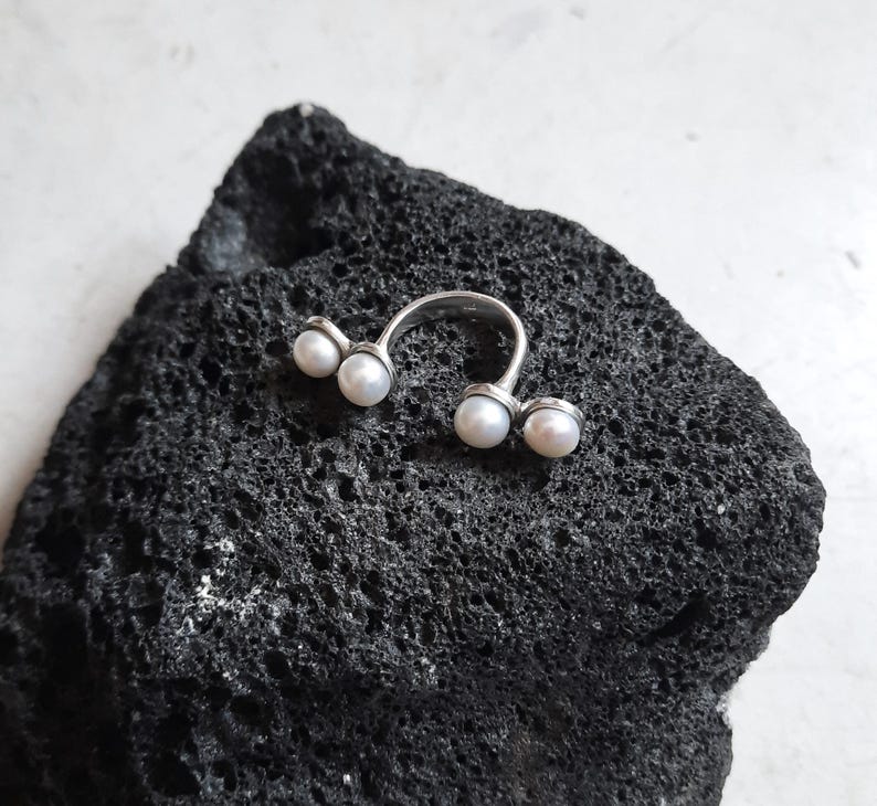 May include: A silver ring with four white pearls set in a curved design.