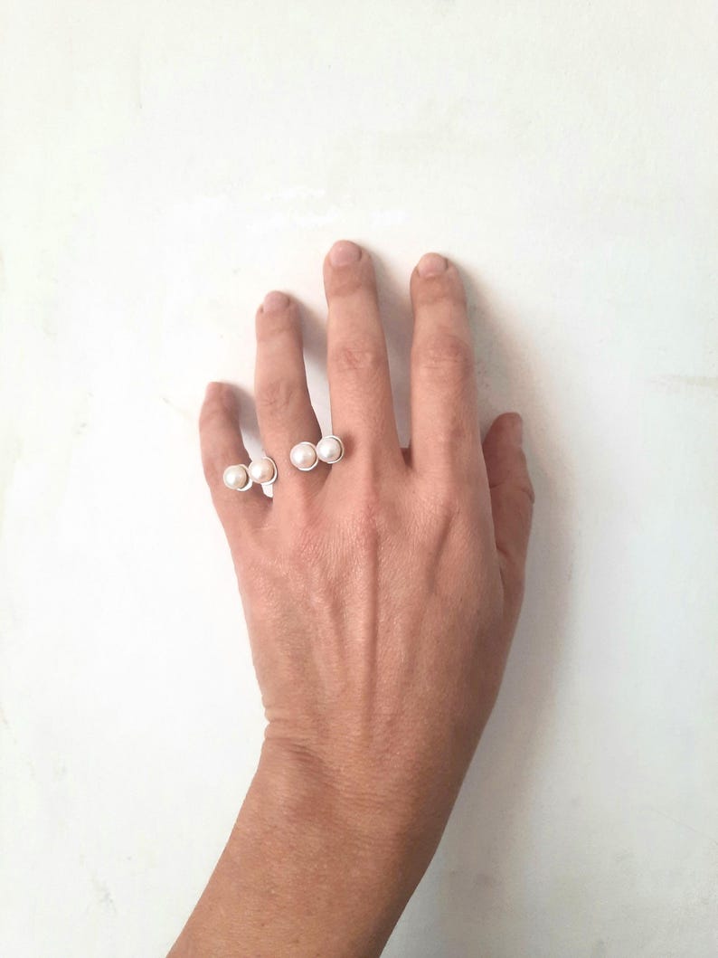 May include: A silver ring with three white pearls on a hand. The ring is designed to be worn on two fingers.