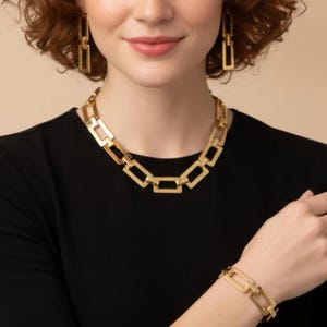 May include: Gold-toned jewelry set featuring a necklace, earrings, and bracelet. The necklace and bracelet have a chain link design. The earrings are rectangular. The woman in the image is wearing a black top.
