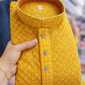 Woman holding a folded embroidered men’s kurta with mandarin collar and textured floral design, displayed in store.