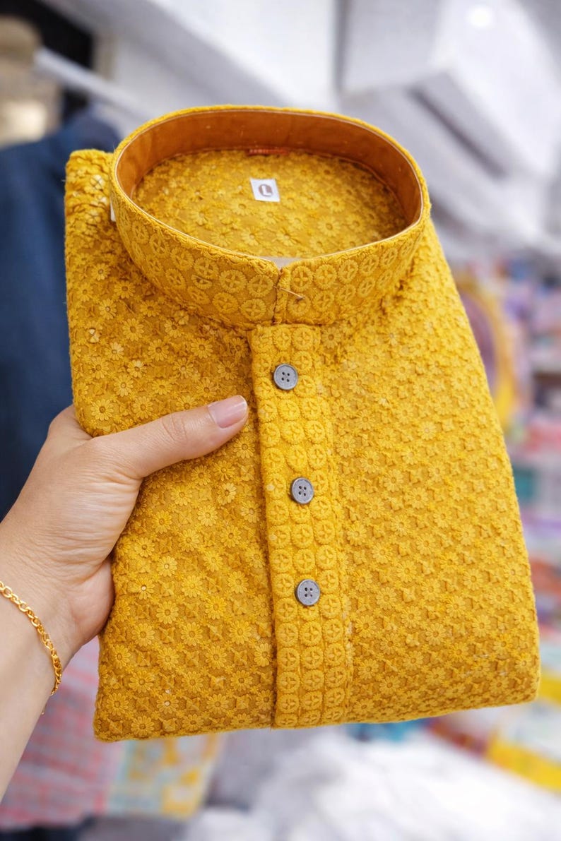Woman holding a folded embroidered men’s kurta with mandarin collar and textured floral design, displayed in store.