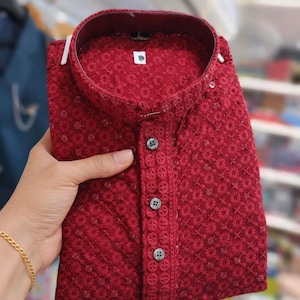 Woman holding a folded embroidered men’s kurta with mandarin collar and textured floral design, displayed in store.