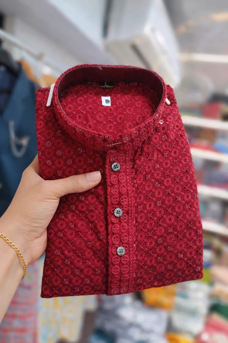 Woman holding a folded embroidered men’s kurta with mandarin collar and textured floral design, displayed in store.